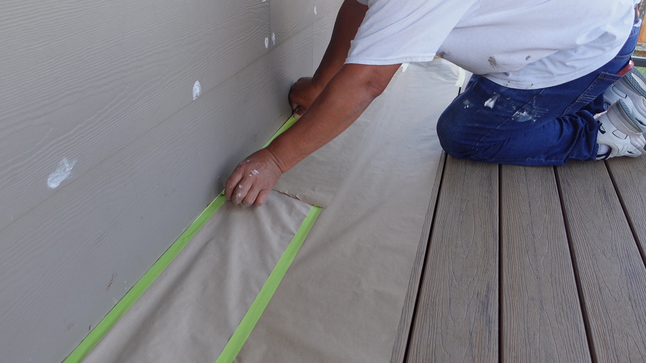 A professional painter in Wichita, KS, carefully taping and masking the exterior siding to prepare for a flawless paint application. This meticulous preparation ensures clean lines and long-lasting results for commercial and residential painting projects.